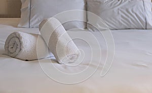 Hotel bedroom. White fluffy, rolled towels, linen sheets and pillows on a bed. Close up view