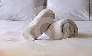 Hotel bedroom. White fluffy, rolled towels, linen sheets and pillows on a bed. Close up view