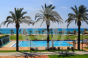 Hotel grounds with swimming pool, clear blue sea and trees, summer Sunny day palm trees