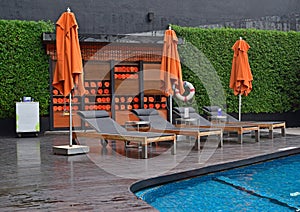 Hotel pool side setup with large umbrella, cushion sundeck chair & rolled towels in cabinet