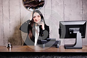 Hotel receptionist. Modern hotel reception desk with bell. Happy female receptionist worker standing at hotel counter and talking