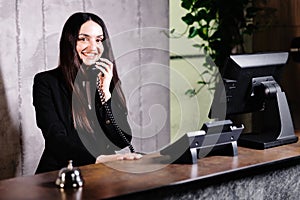 Hotel receptionist. Modern hotel reception desk with bell. Happy female receptionist worker standing at hotel counter and talking