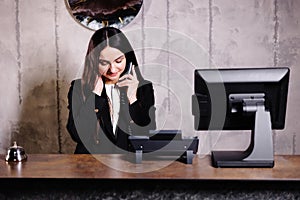 Hotel receptionist. Modern hotel reception desk with bell. Happy female receptionist worker standing at hotel counter and talking