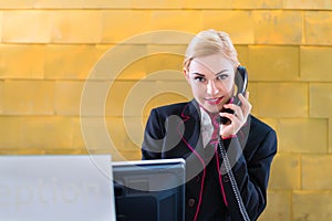 Hotel receptionist with phone on front desk