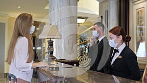 Hotel receptionists wearing medical masks, checking in young woman at the hotel room