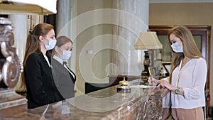 Hotel receptionists wearing medical masks, checking in young woman at the hotel room