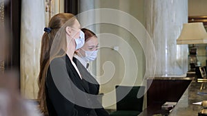 Hotel receptionists wearing medical masks, checking in young woman at the hotel room