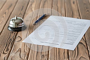 Hotel reservation form and silver vintage bell on wooden rustic reception desk. Hotel service, registration. Selective focus.