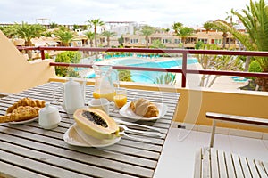 Hotel room breakfast on balcony view of swimming pool and palm trees. Vacation travel morning food breakfast in luxury resort