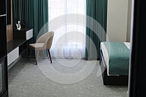 The hotel room interior with a gray armchair in front of a black and white dresser