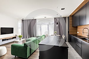 Hotel room interior with green lounge, TV set, windows with drapes and open space kitchen corner