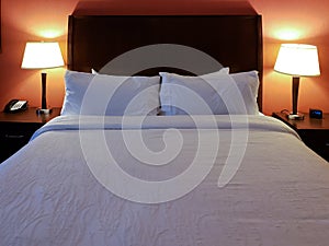 Hotel room interior with made bed and pillows with lamps on and a red wall