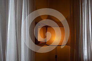 Hotel room with orange lit abat-jour, framed mirror and white curtains photo