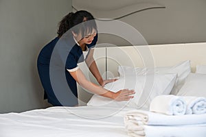 Hotel room service. Young Asian woman maid making bed in guest room