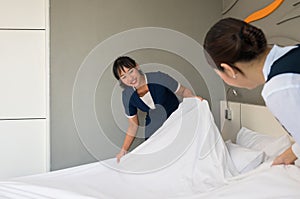 Hotel room service. Young two Asian woman maid in uniform making bed in guest room