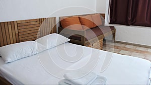 A hotel room with a white double bed, brown sofa with orange cushions and chocolate curtains