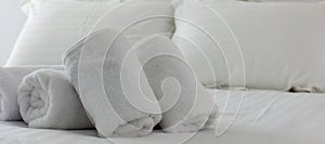 Hotel`s bedroom. White fluffy, rolled towels, linen sheets and pillows on a bed. Close up view.