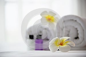 Hotel towel and shampoo and soap bath bottle set on white bed with plumeria flower decorated