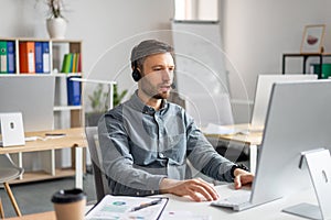 Hotline support service. Handsome mature male call center operator in headset working on modern computer in office