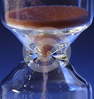 Hour Glass with running sand inside, on blue background. Time passing or countdown concept