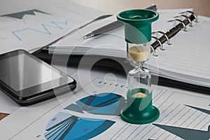Hourglass on the background of the chart,pen, diary, phone.