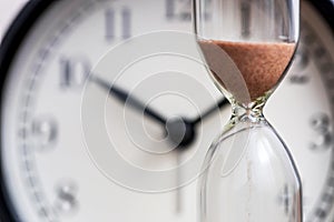 Hourglass on the background of office watch as time passing concept for business deadline, urgency and running out of time. Sand photo