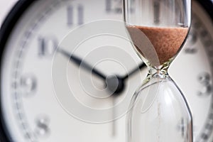 Hourglass on the background of office watch as time passing concept for business deadline, urgency and running out of time. Sand