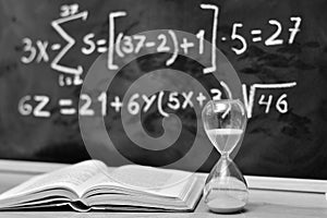 Hourglass and book on a table, with a blackboard background