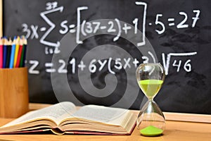 Hourglass and book on a table, with a blackboard background