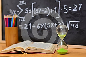 Hourglass and book on a table, with a blackboard background photo