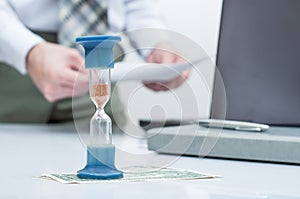 Hourglass. Businessman working in the office in the background. Concept time is money.