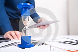 Hourglass. Businessman working in the office in the background. Concept time is money.