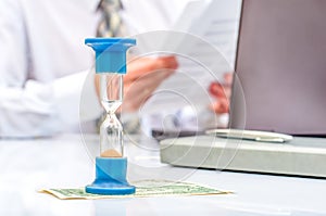 Hourglass. Businessman working in the office in the background. Concept time is money.