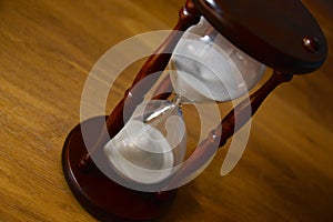 Hourglass, clock in front of wooden background with copy space. Closeup.