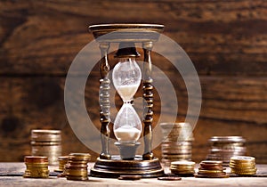 Hourglass and coins on wooden background