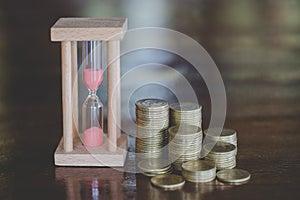 Hourglass with coins on wooden background, Time investment and retirement saving. Urgency countdown timer for business deadline