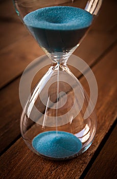 Hourglass containing blue sand on a rustic wooden board