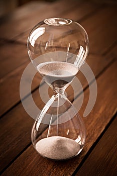 Hourglass containing white sand on a rustic wooden board