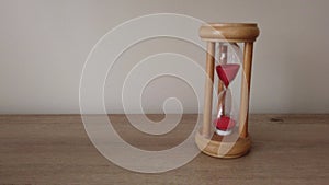 Hourglass countdown sand falls in a sandglass on wood desk. Passing time concept.