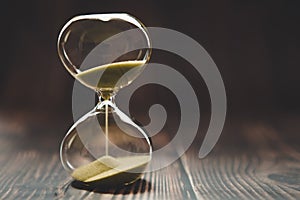 Hourglass with falling sand inside a glass bulb, passing time or lost time on a dark background with space for text
