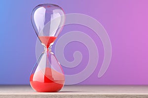 Hourglass with flowing red sand on table against color background, space for text