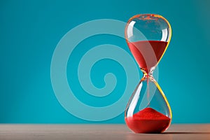 Hourglass with flowing red sand on table against light blue background, space for text