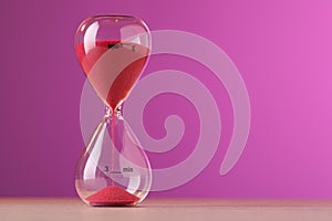 Hourglass with flowing red sand on table against violet background, space for text
