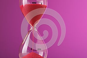 Hourglass with flowing red sand on violet background, closeup. Space for text