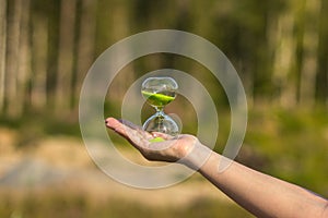 Hourglass with green sand on the palm of the girl on a blurred background