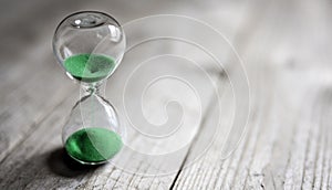 Hourglass with green sand time passing background concept for business deadline, urgency and running out of time