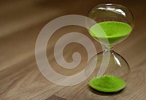 Hourglass with green sand on a wooden background