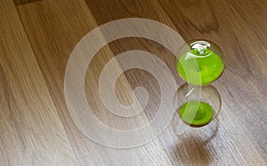 Hourglass with green sand on a wooden surface, top view