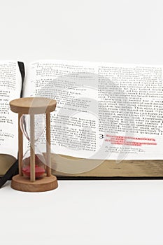 Hourglass and open bible on the book of Ecclesiastes with selective focus on verse 1 of chapter 3 highlighted in red. Isolated on