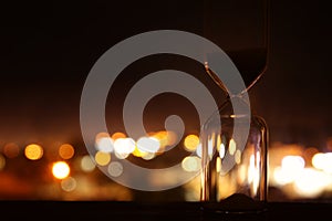 Hourglass over bokeh city lights as time passing concept for business deadline.